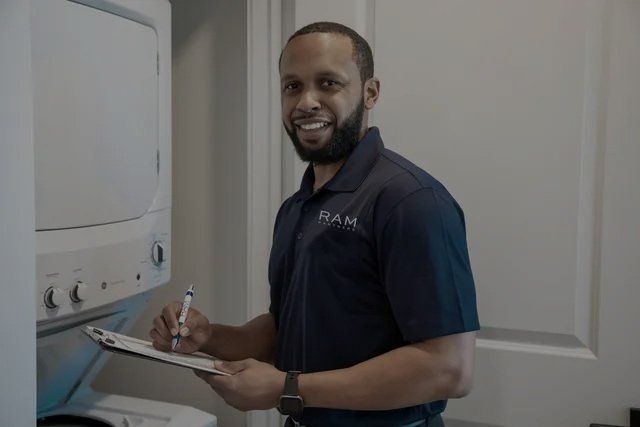 A man is standing in front of a washer and dryer holding a clipboard and a pen.