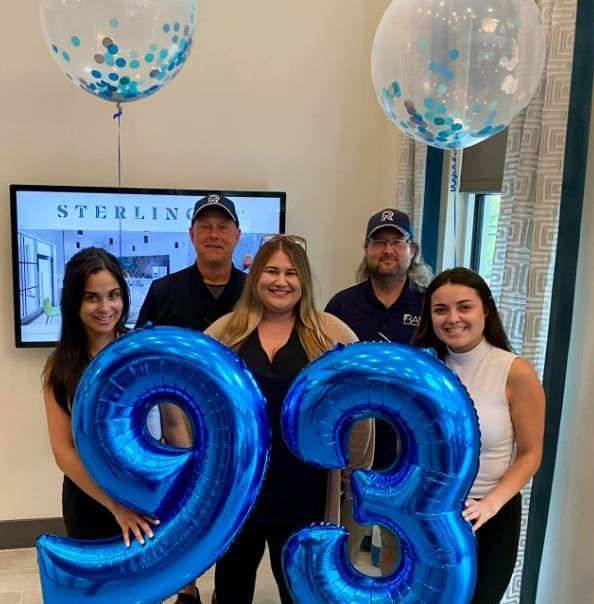A group of people holding blue balloons in the shape of the number 93