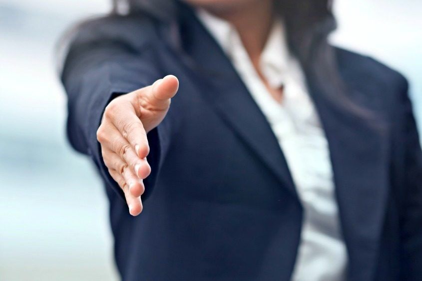 A woman in a suit is reaching out her hand to shake someone 's hand.