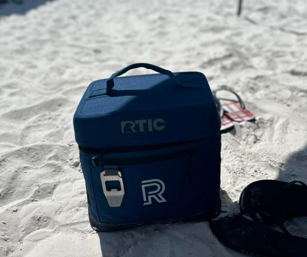 A blue rtic bag is sitting on a sandy beach