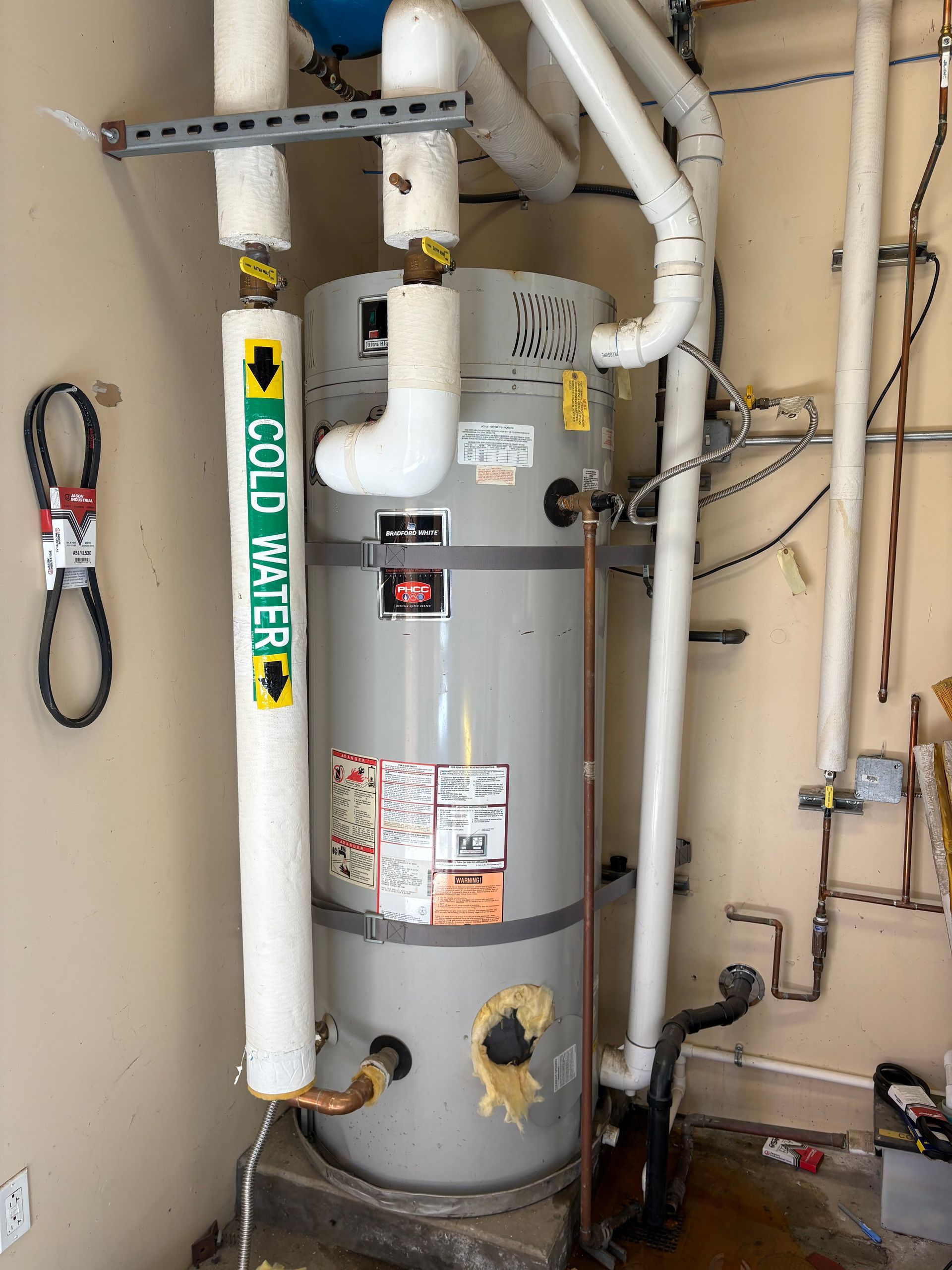 A grey water heater in a room, with insulated cold water pipes and electrical wiring on the wall.