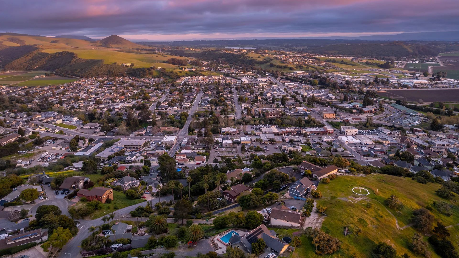 A person sits on a rock in a calm sea during a vibrant orange and purple sunset.