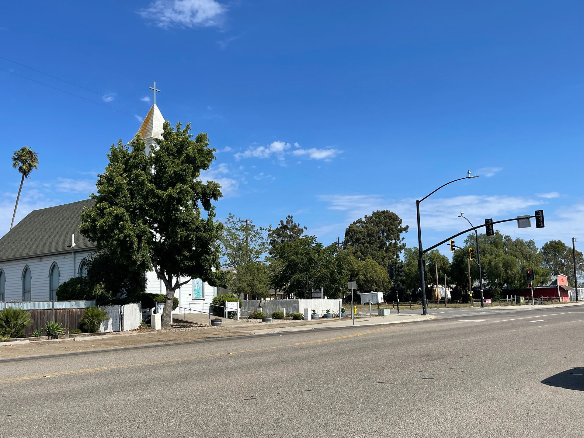An outdoor plaza with terracotta-colored buildings, patio seating, and potted shrubs lining a paved walkway.