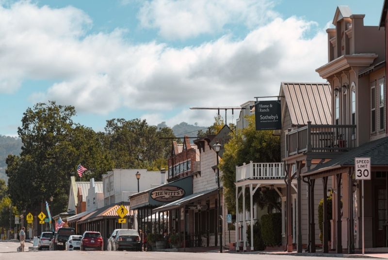 An aerial view of a deep blue lake meeting a snow-covered, pine-forested coastline under a clear, bright blue sky.