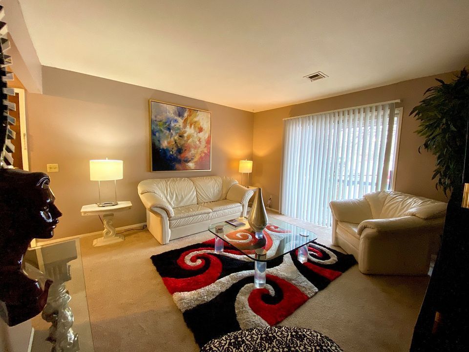 Living room with cream-colored sofas, colorful rug, and abstract art above the couch, near a sliding door.