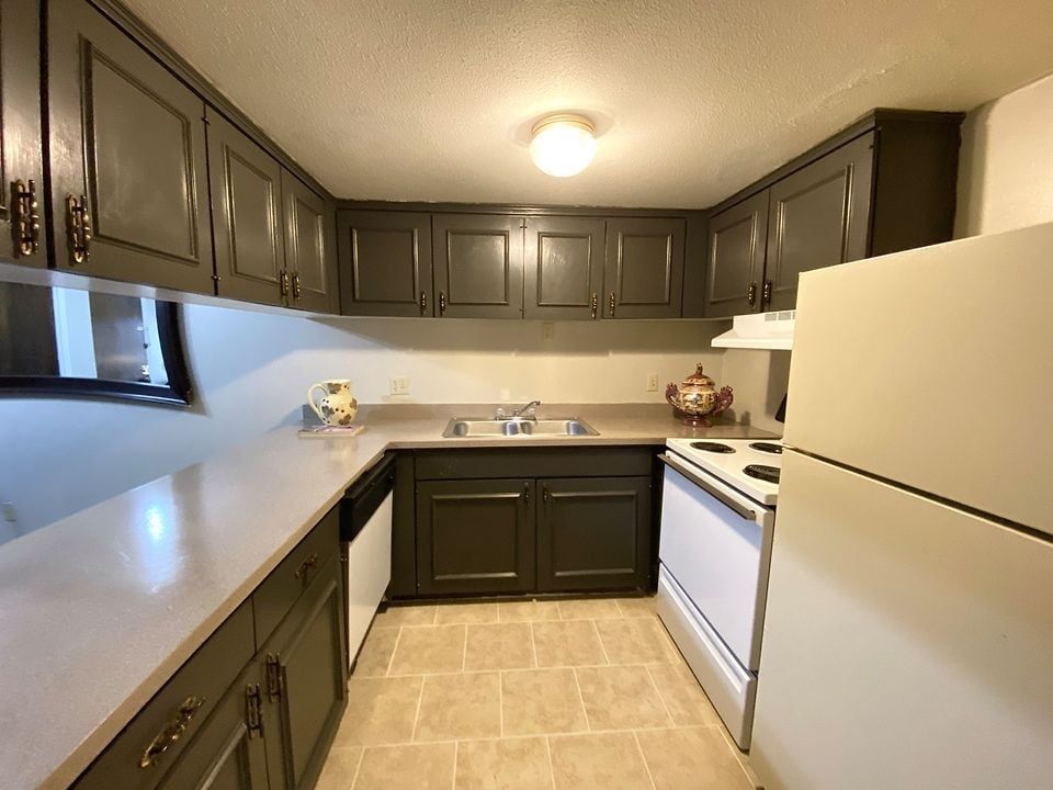 Kitchen with dark cabinets, white appliances, and a tan countertop.
