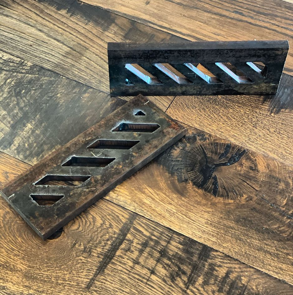 Two metal pieces are sitting on a wooden floor.