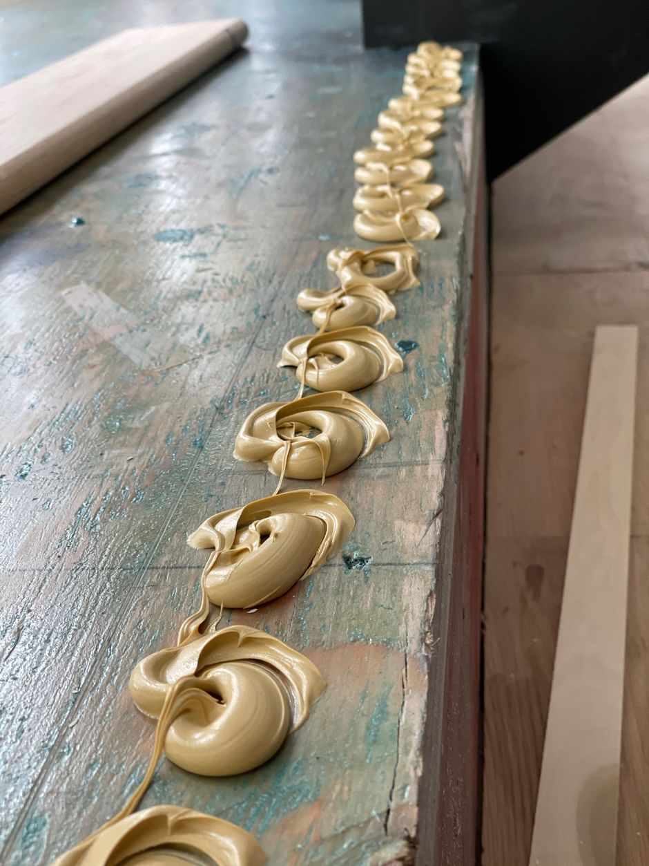 A row of swirls of glue are sitting on a wooden table.