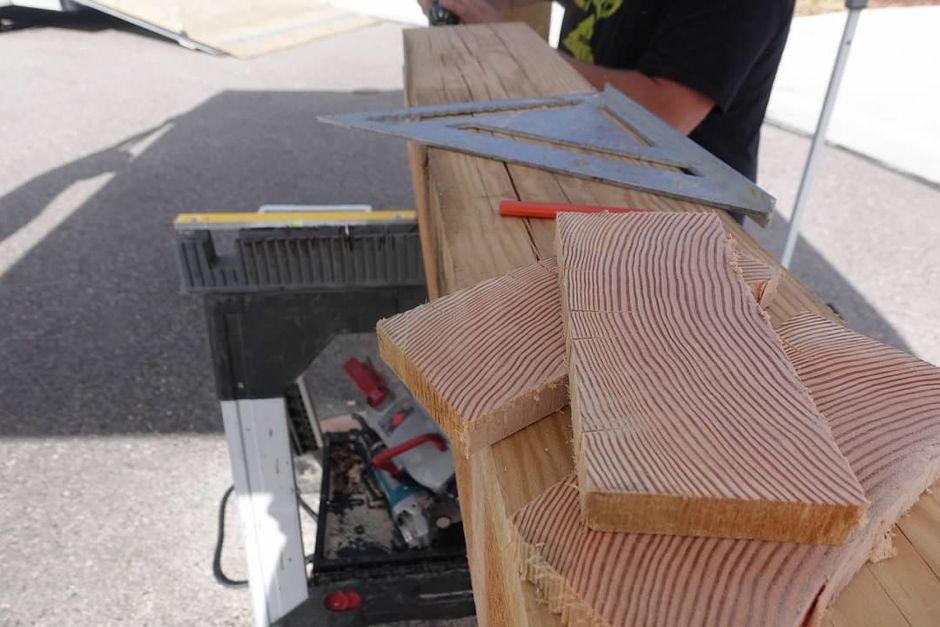 A man is measuring a piece of wood with a triangle