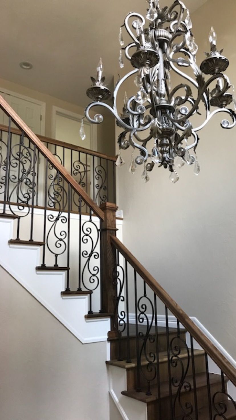 A staircase with a wrought iron railing and a chandelier hanging from the ceiling.