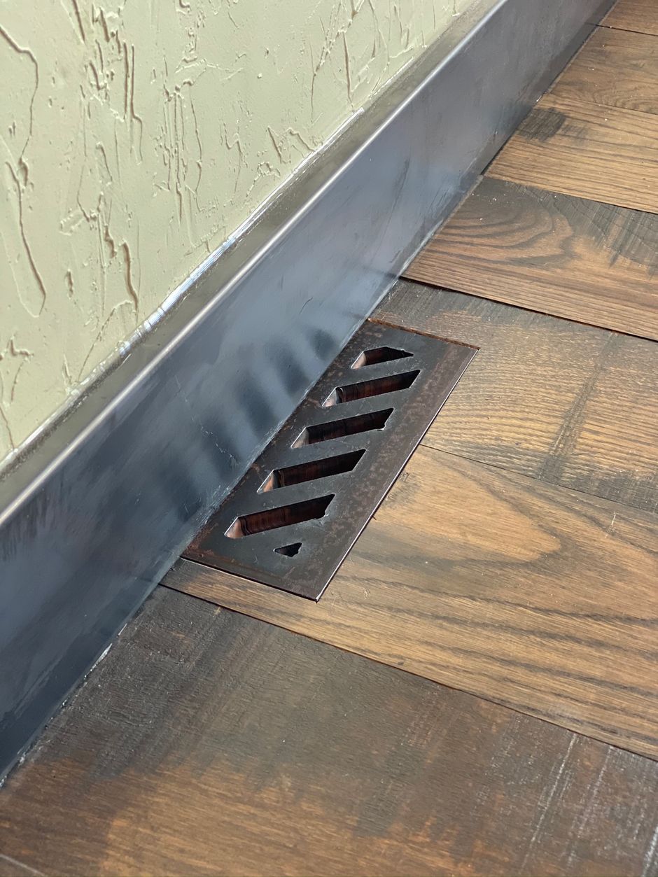 A close up of a vent on a wooden floor next to a wall.