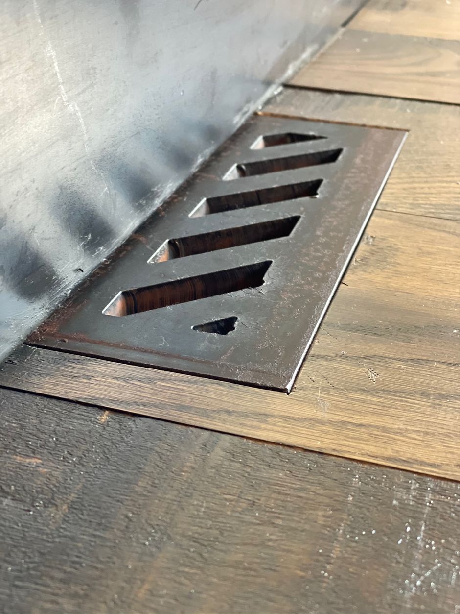 A metal drain is sitting on a wooden floor next to a wall.