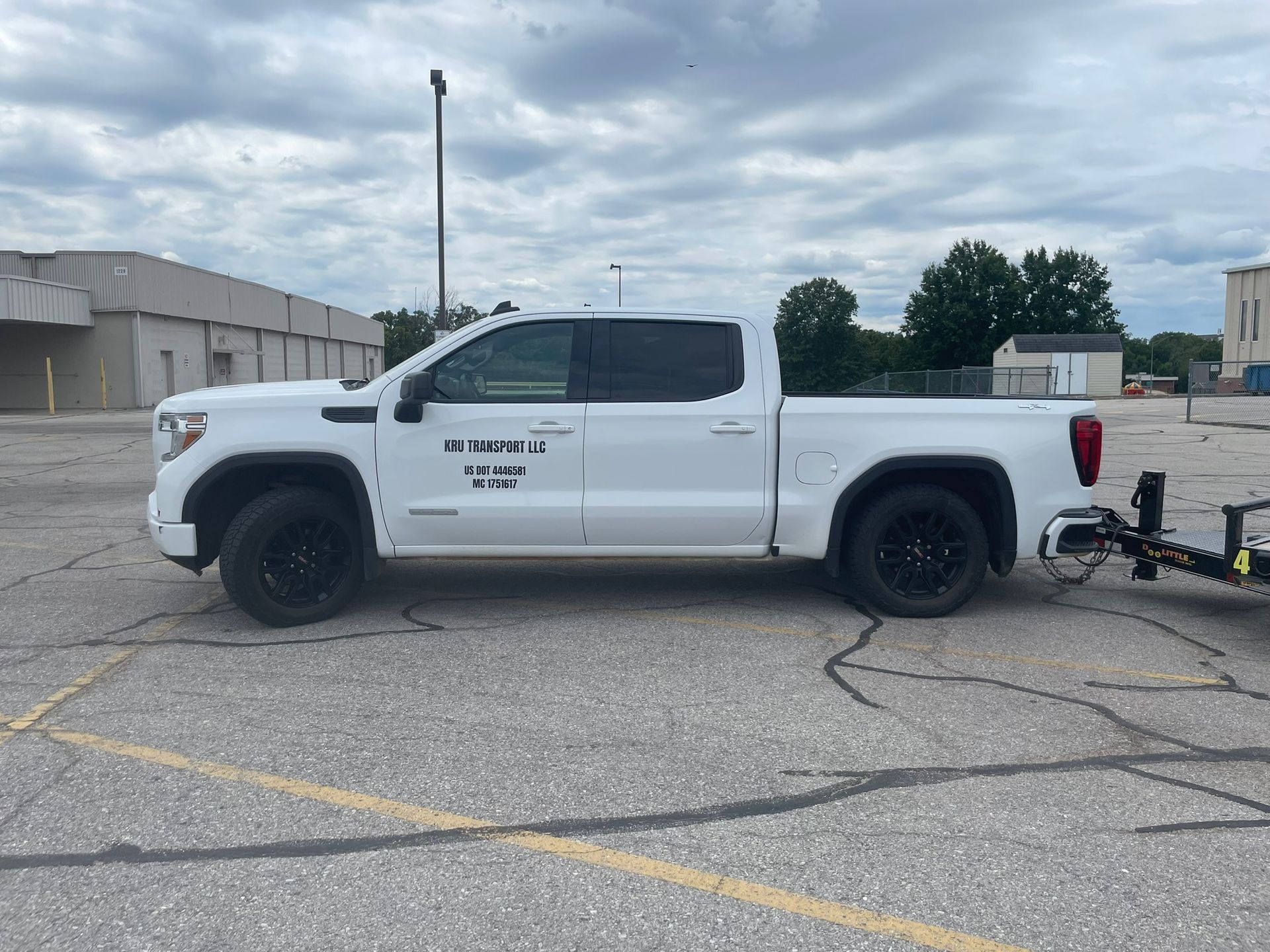 White pickup truck with black wheels pulling a trailer in a parking lot; cloudy sky.