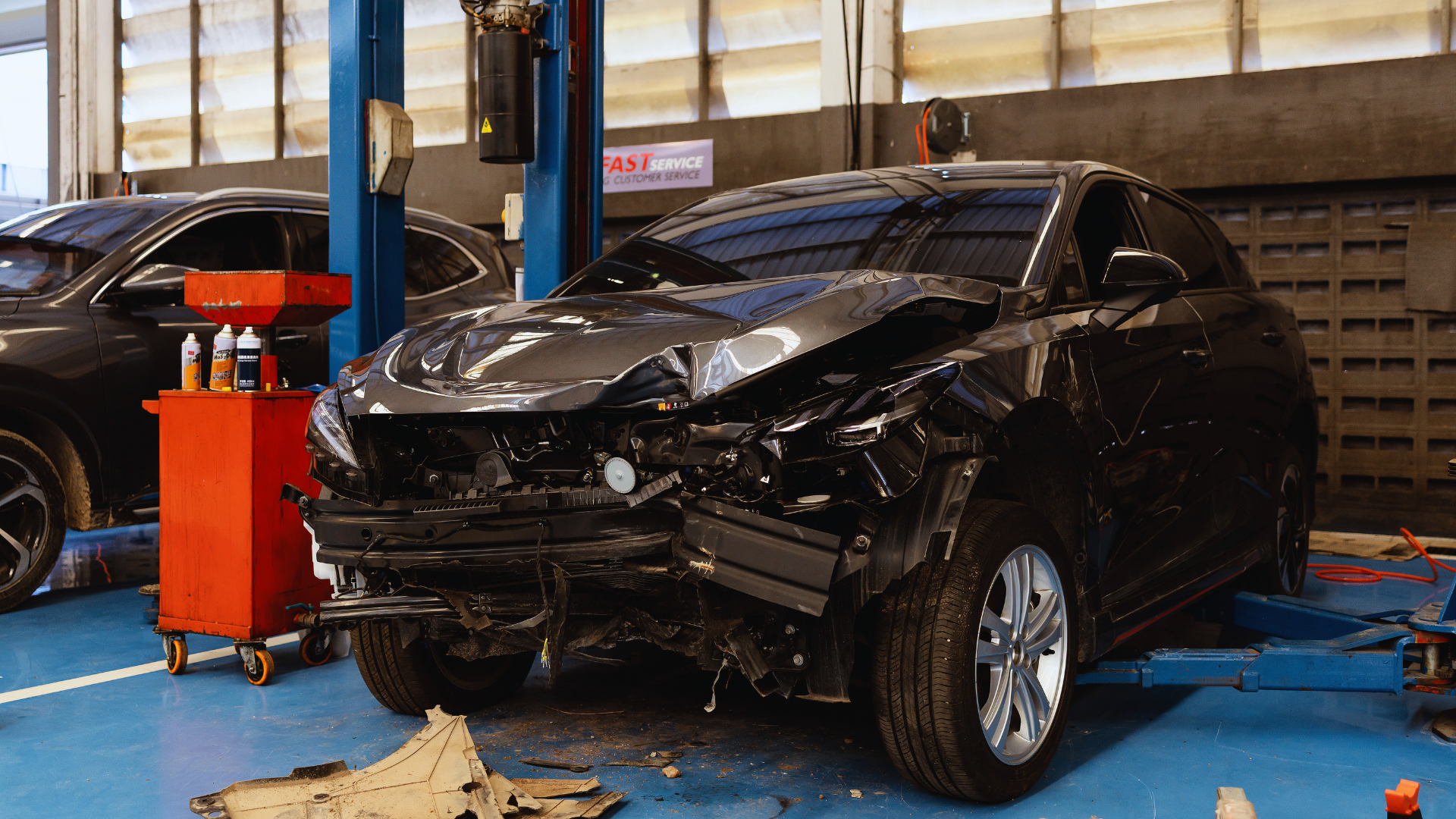 Black car with severe front-end damage in an auto repair shop, on a lift with tools nearby