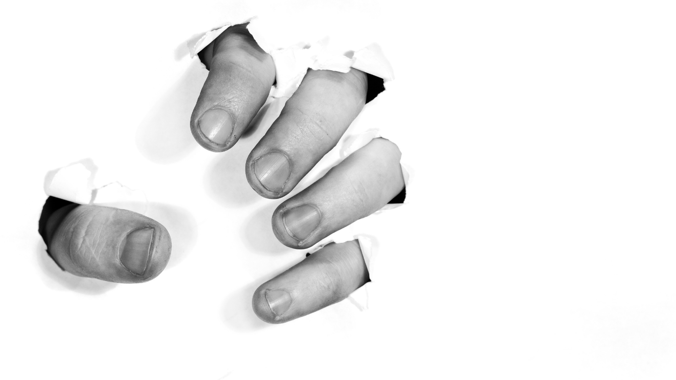 A hand with fingers poking through torn holes in white paper.