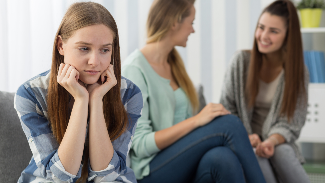 Woman looking sad while two others laugh nearby.