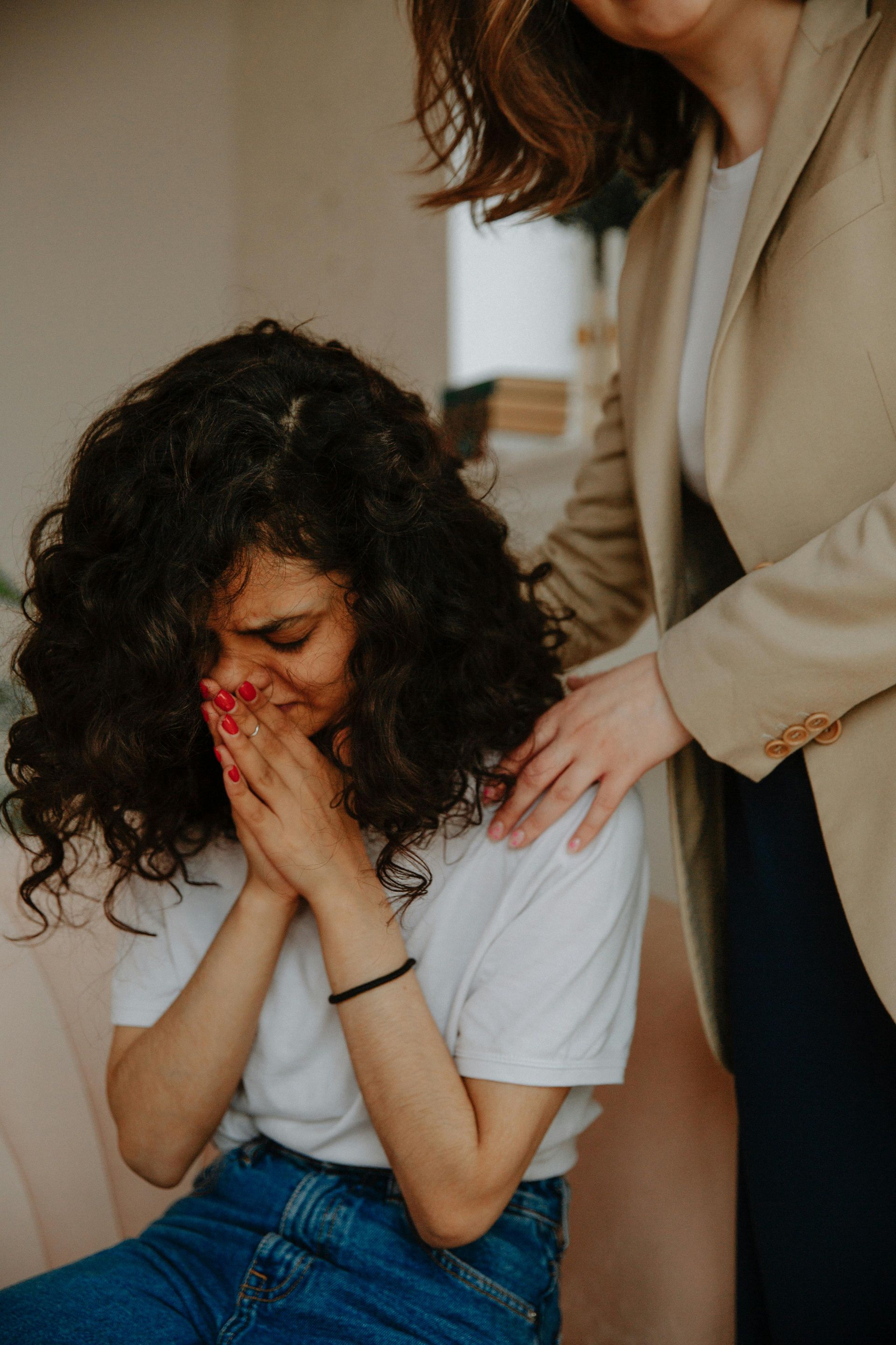 Woman crying, consoled by another woman who has hand on her shoulder; interior setting.