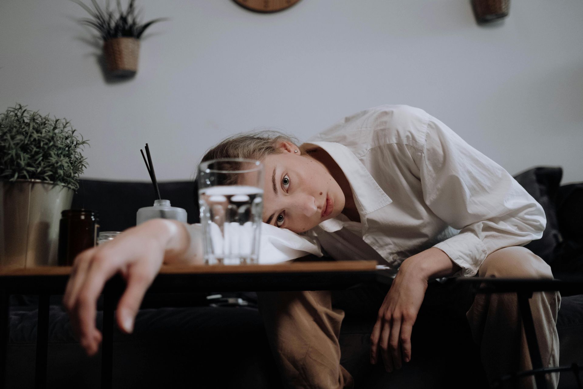 Woman in white leaning on a table, appearing sad and emotionally distressed.