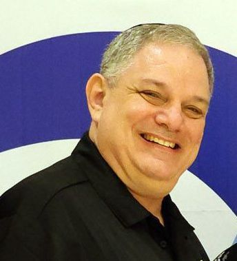 A man in a black shirt is smiling in front of a palm tree.