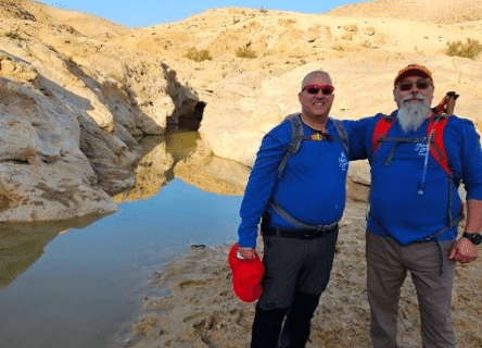 Two men are standing next to each other in front of a body of water.