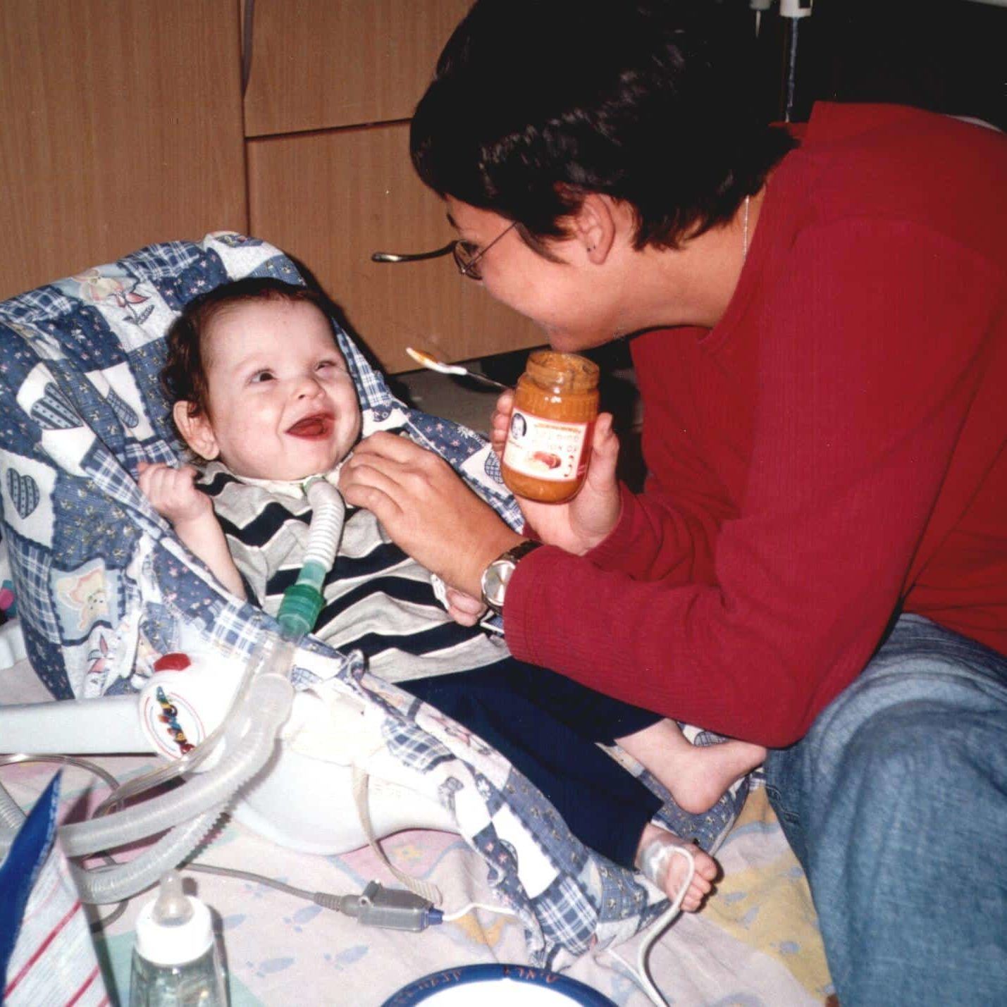 A woman in a red shirt is feeding a baby in a high chair
