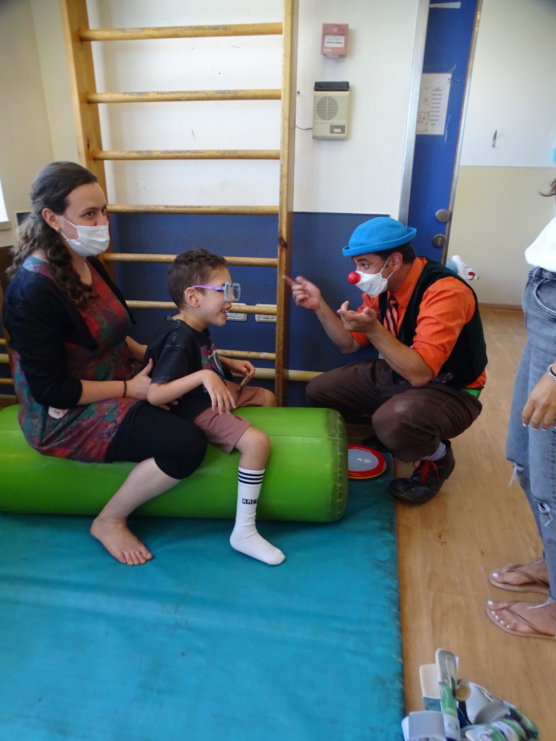 A woman is sitting on a green roll next to a clown and a child.