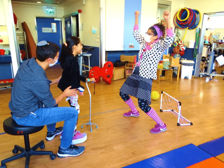 A man sits on a stool watching a girl in pink socks dance