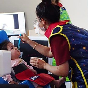A woman is feeding a baby in a chair with a spoon.