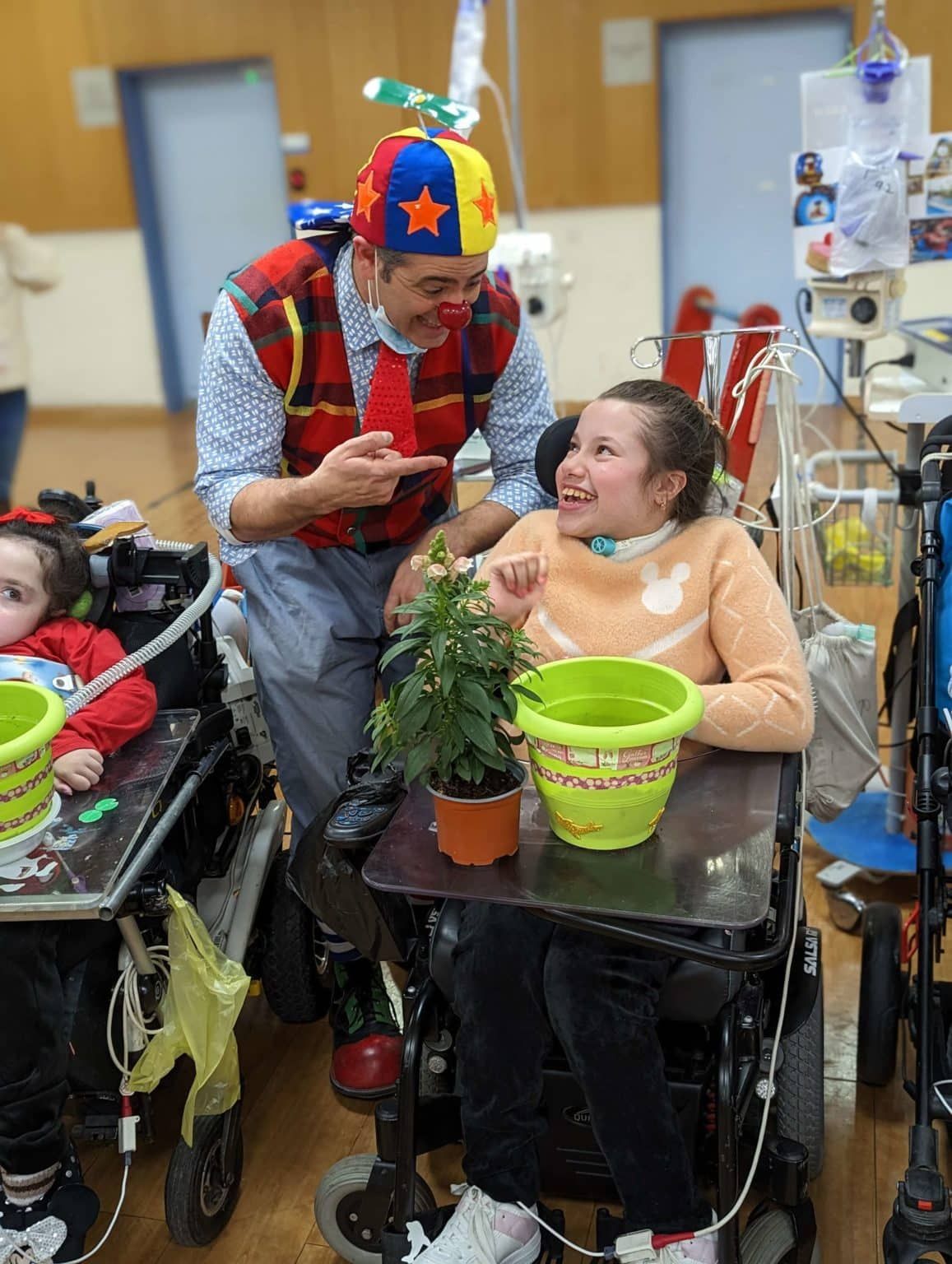 A man in a clown costume is talking to a girl in a wheelchair.