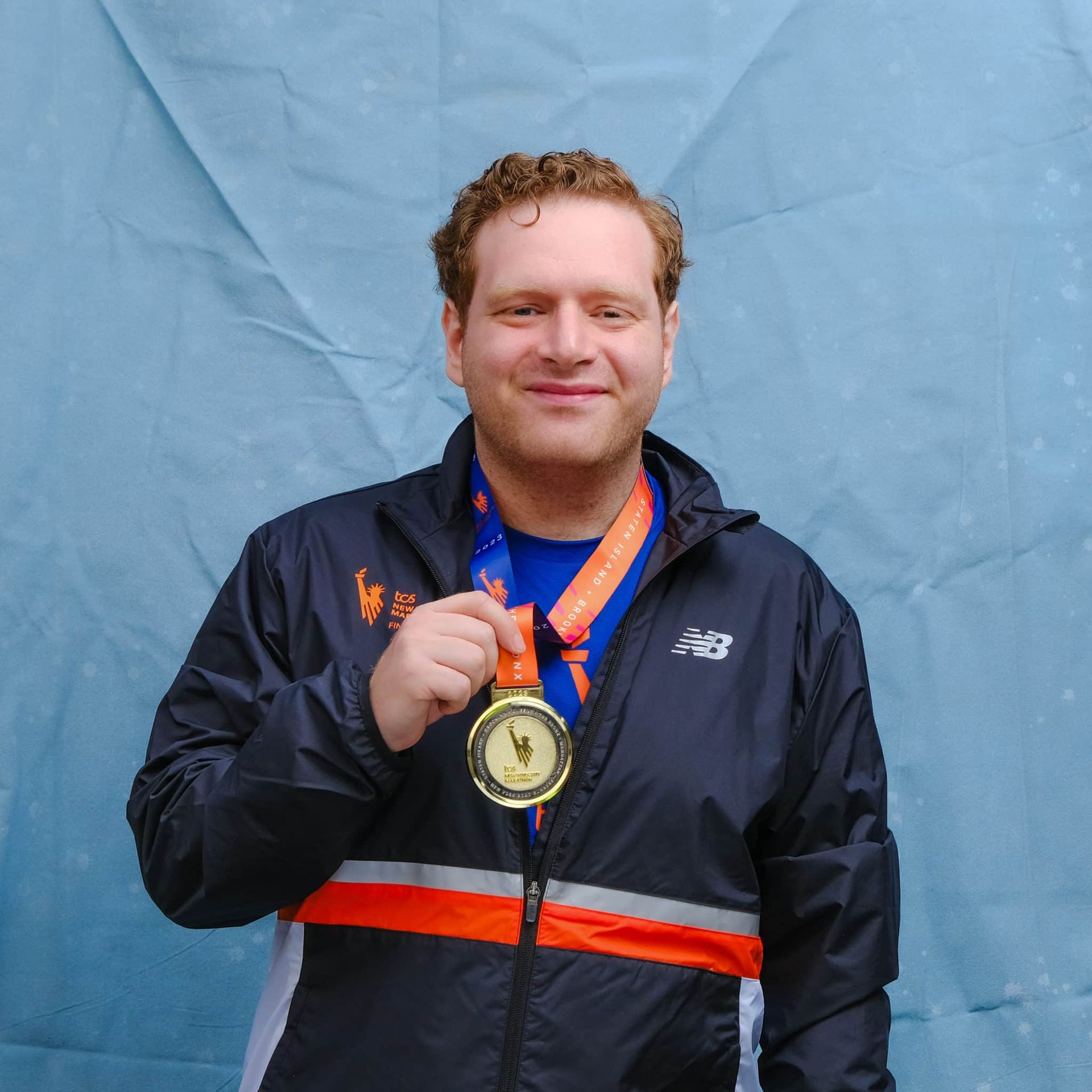 A man wearing a new balance jacket is holding a medal
