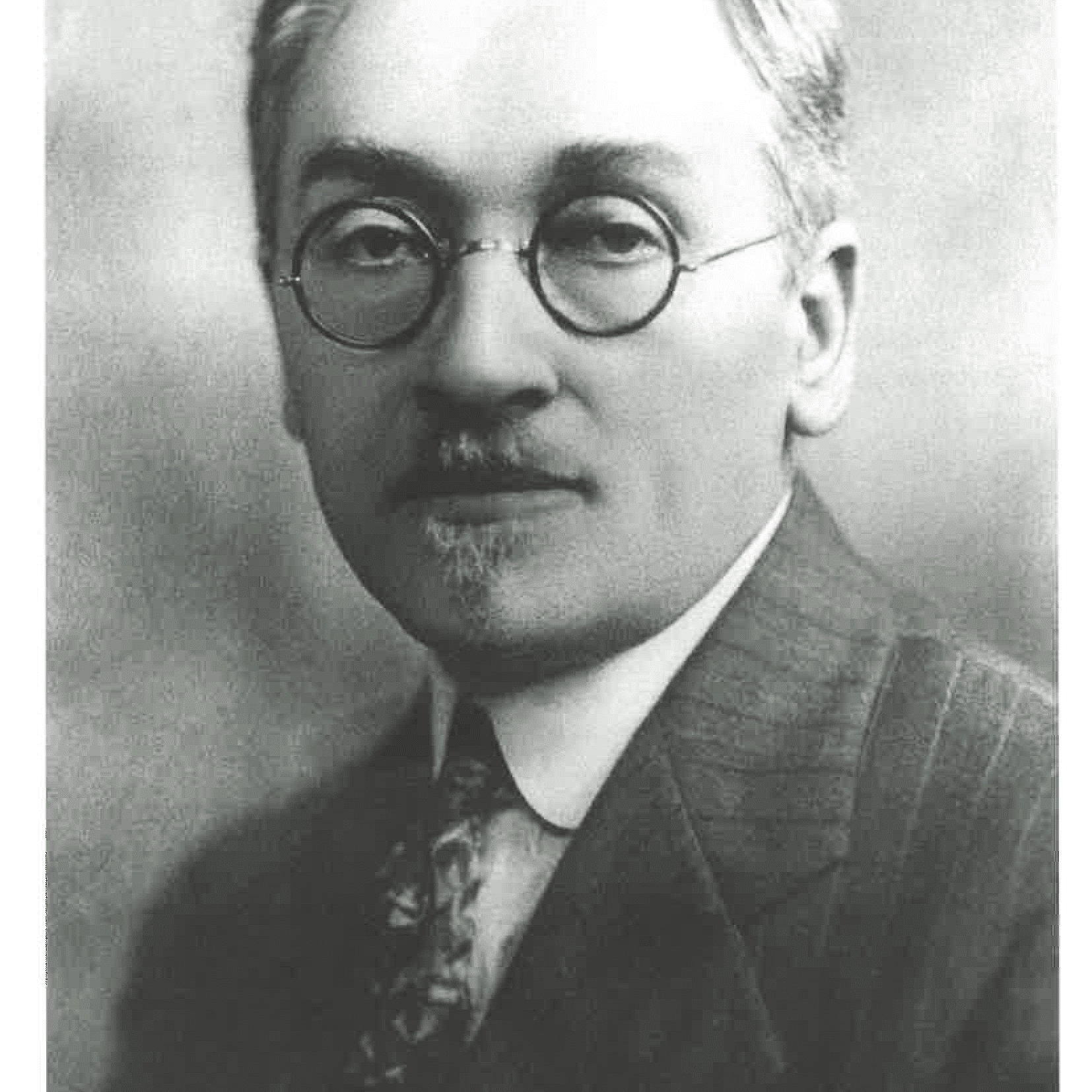 A black and white photo of a man wearing glasses and a suit and tie.