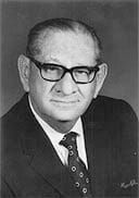 A black and white photo of a man wearing glasses and a suit and tie.