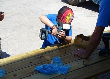 A young boy is using a drill on a wooden table.