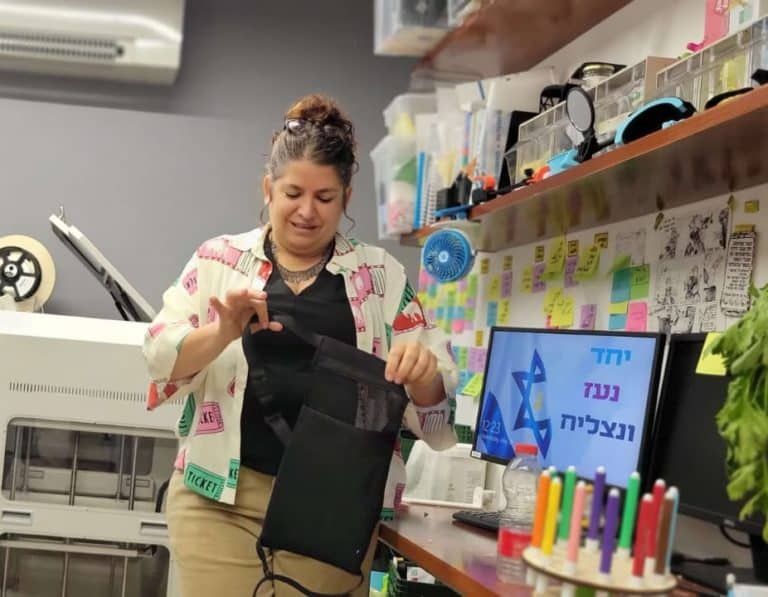 A woman is standing in front of a computer and holding a tablet.