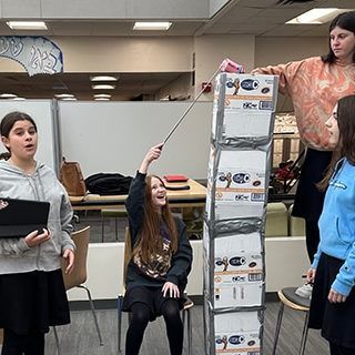 A group of young girls are standing around a stack of boxes.