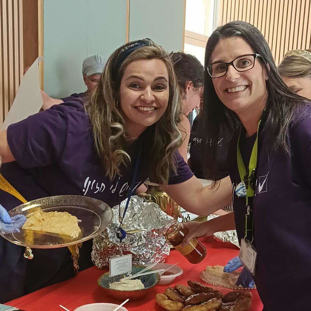 Two women are standing next to each other holding plates of food.