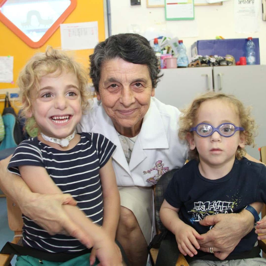 A woman in a lab coat holds two young children