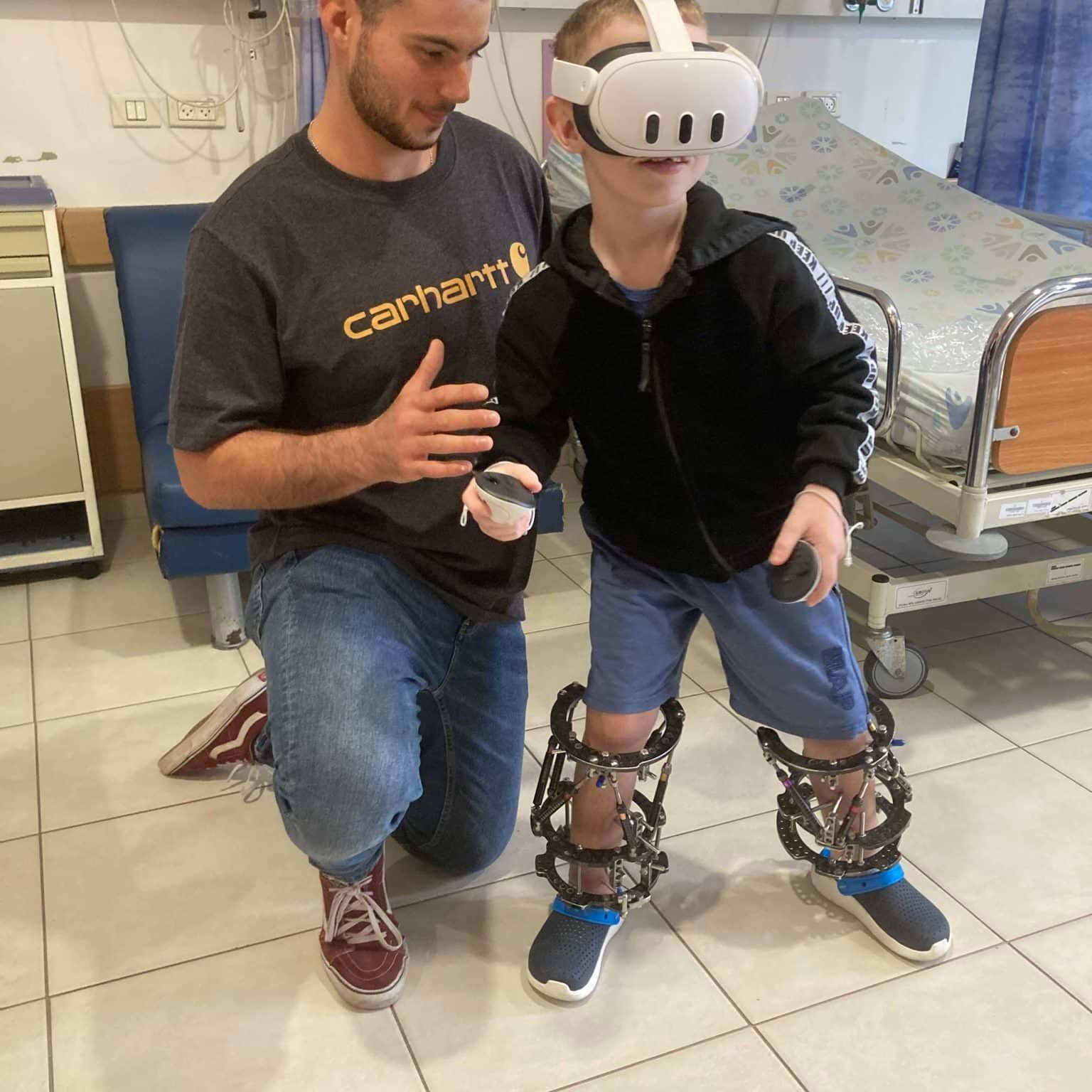 A man wearing a carhartt shirt is kneeling next to a boy wearing a virtual reality headset