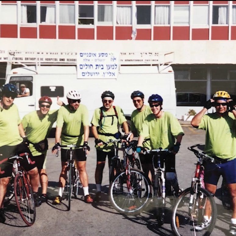 A group of cyclists are posing for a photo in front of a building with a sign that says ' a ' on it