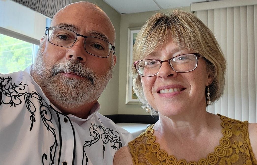 A man and a woman are posing for a picture together . the woman is wearing glasses.