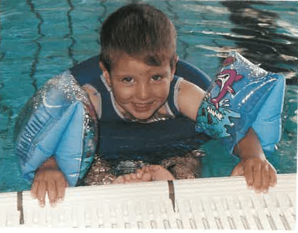A young boy is swimming in a pool wearing a life jacket and arm floats.