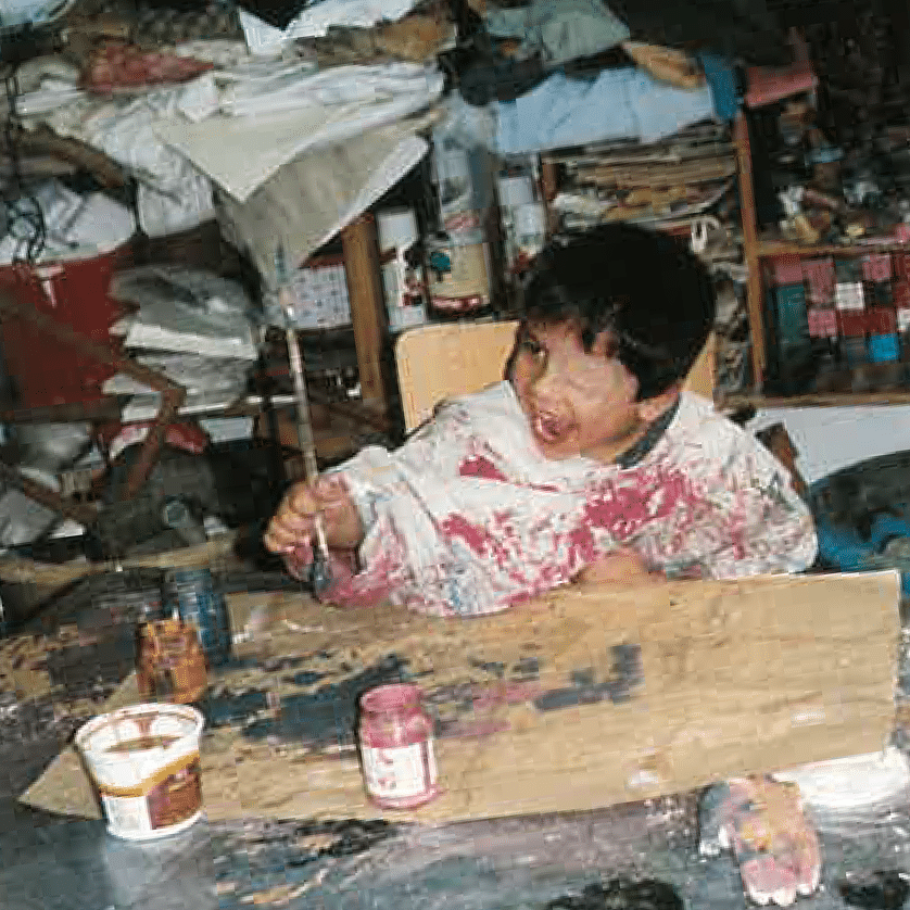 A young boy is sitting at a table covered in paint.