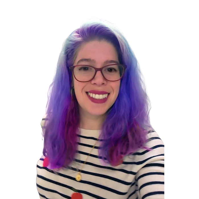 A woman with blue and purple hair is wearing glasses and a pink sweater.
