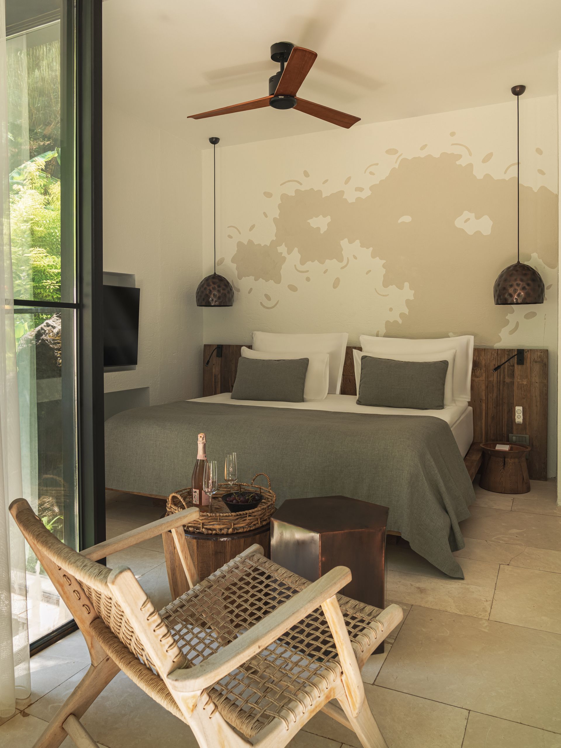 A modern bedroom featuring a bed with gray bedding, a rustic wooden chair in the foreground, and a wall with painted detail.