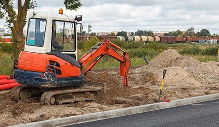 A small orange and white excavator is digging a hole in the dirt.