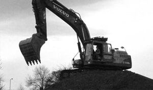 A black and white photo of a volvo excavator on top of a pile of dirt.