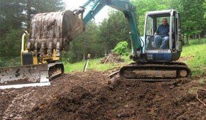 A man is driving an excavator and a bulldozer in a dirt field.