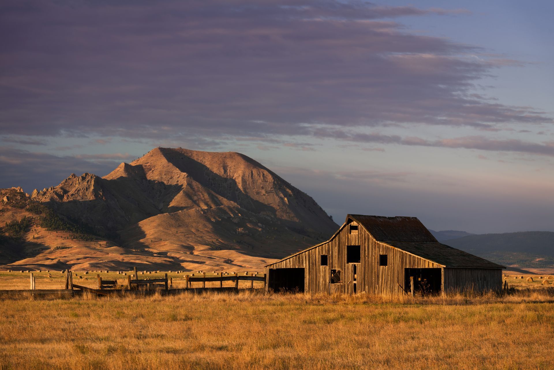 an old barn is sitting in the middle of a field with mountains in the background .