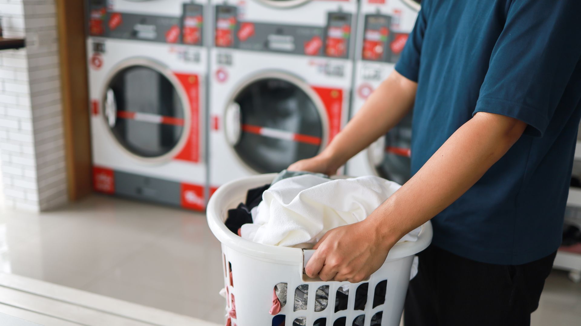 a man is holding a laundry basket full of clothes in a laundromat .