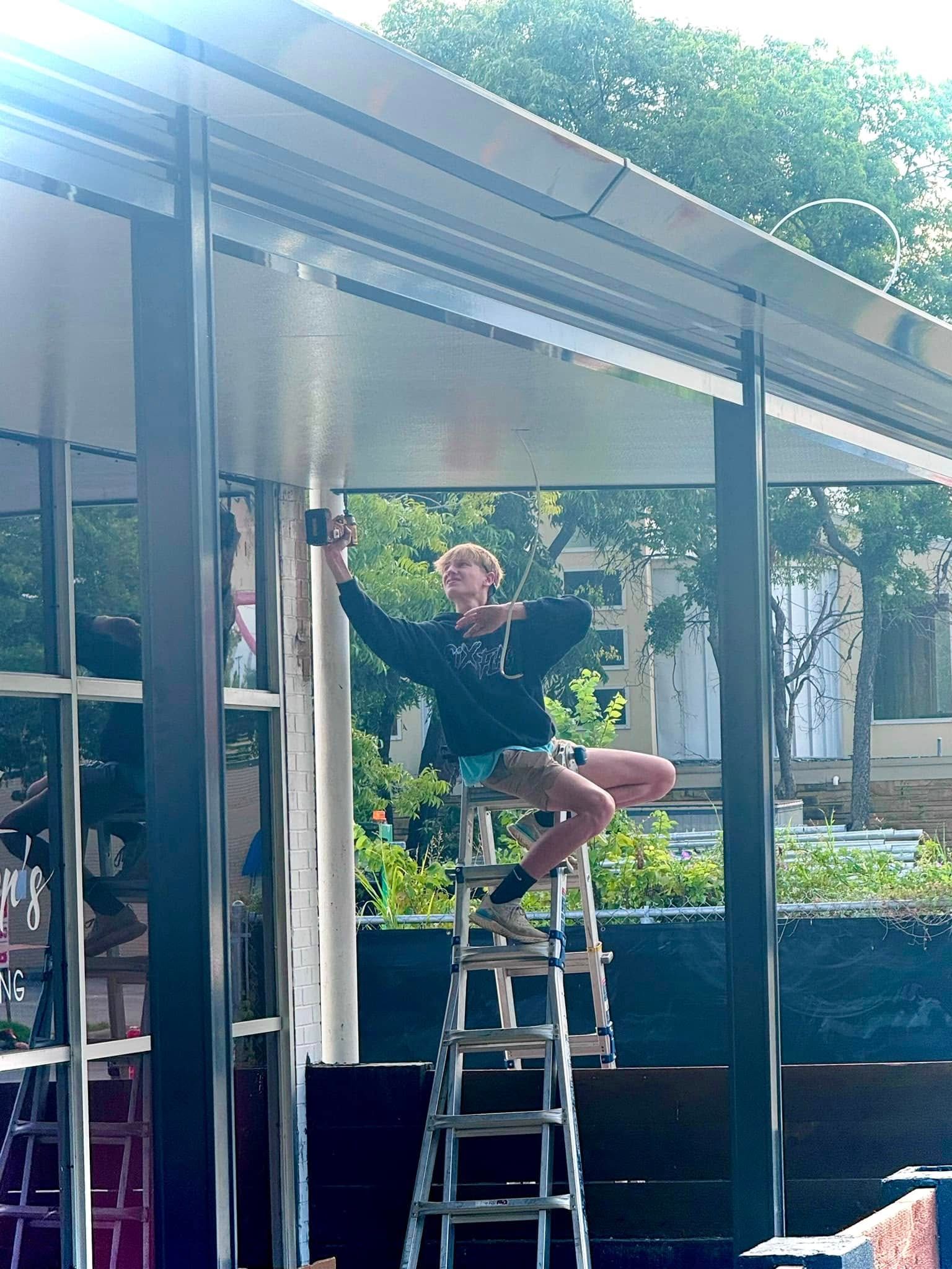 A woman is sitting on a ladder working on a building.